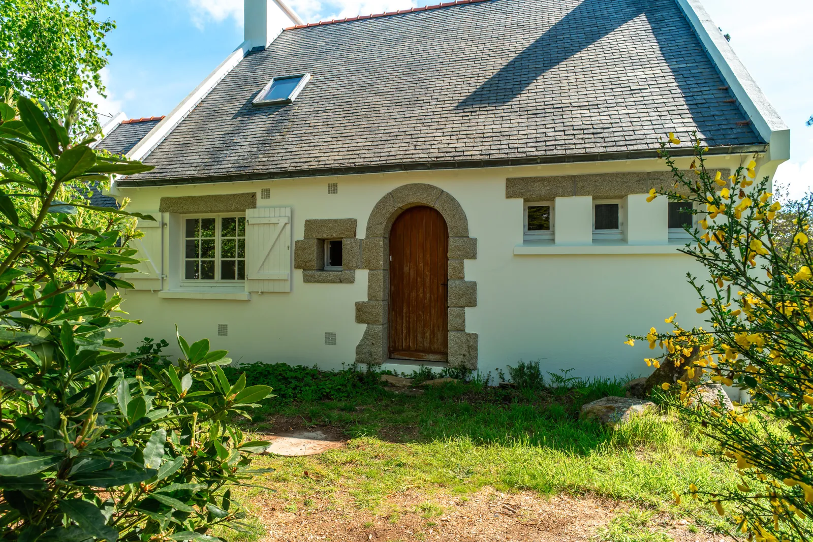 Façade de la maison et sa porte en arche, sous les arbres